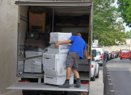 Chargement d’un camion de déménagement d’entreprise avec un employé déplaçant un piano/électroménager volumineux dans une rue. Check-list déménagement entreprise intégrée naturellement.